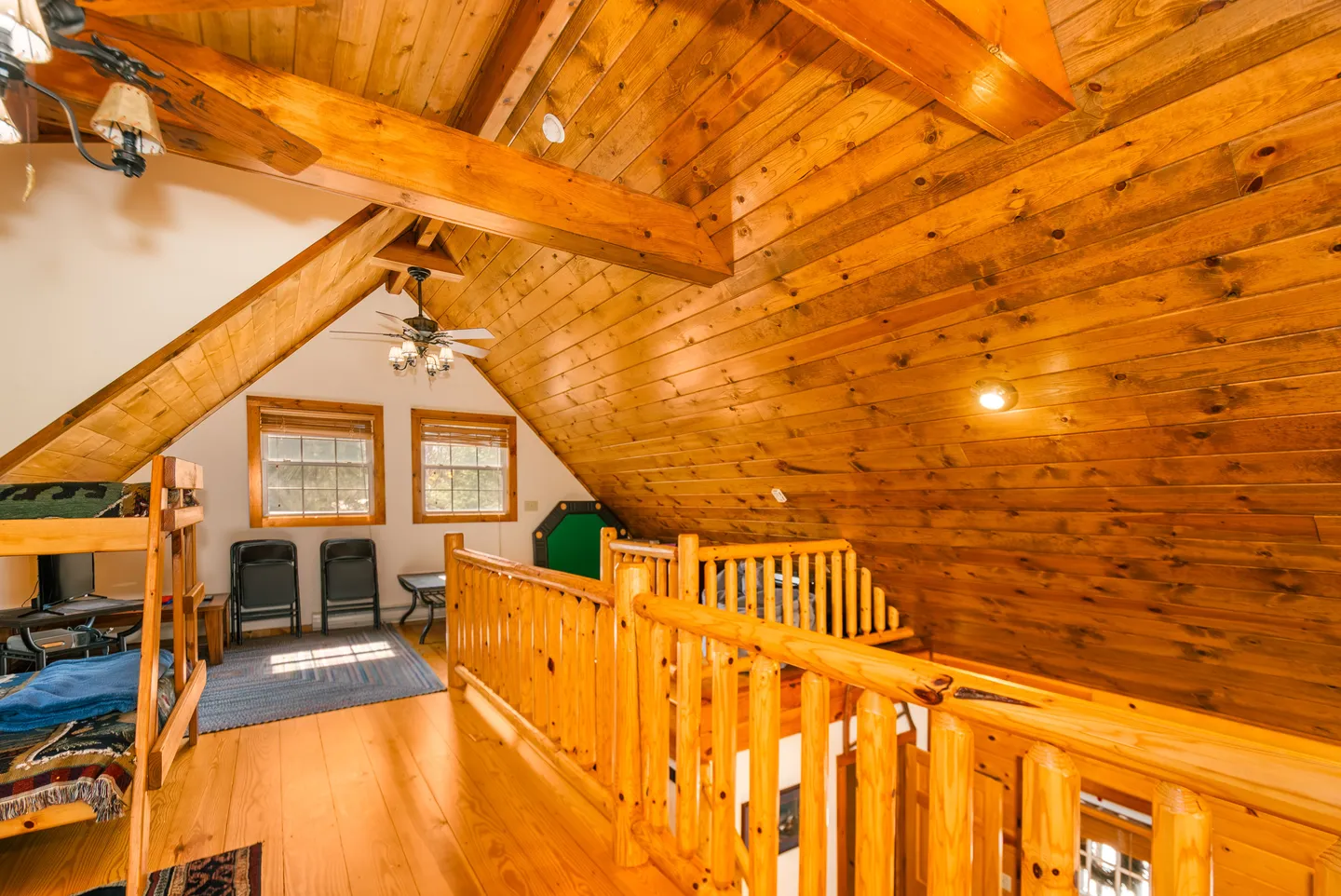 Upstairs cabin loft with wood-paneled ceiling, exposed beams, log railings, and a bunk bed.