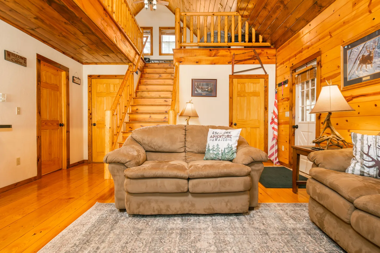 Living room with wooden walls, wood flooring, a brown loveseat, and a wooden staircase leading to an upper loft.