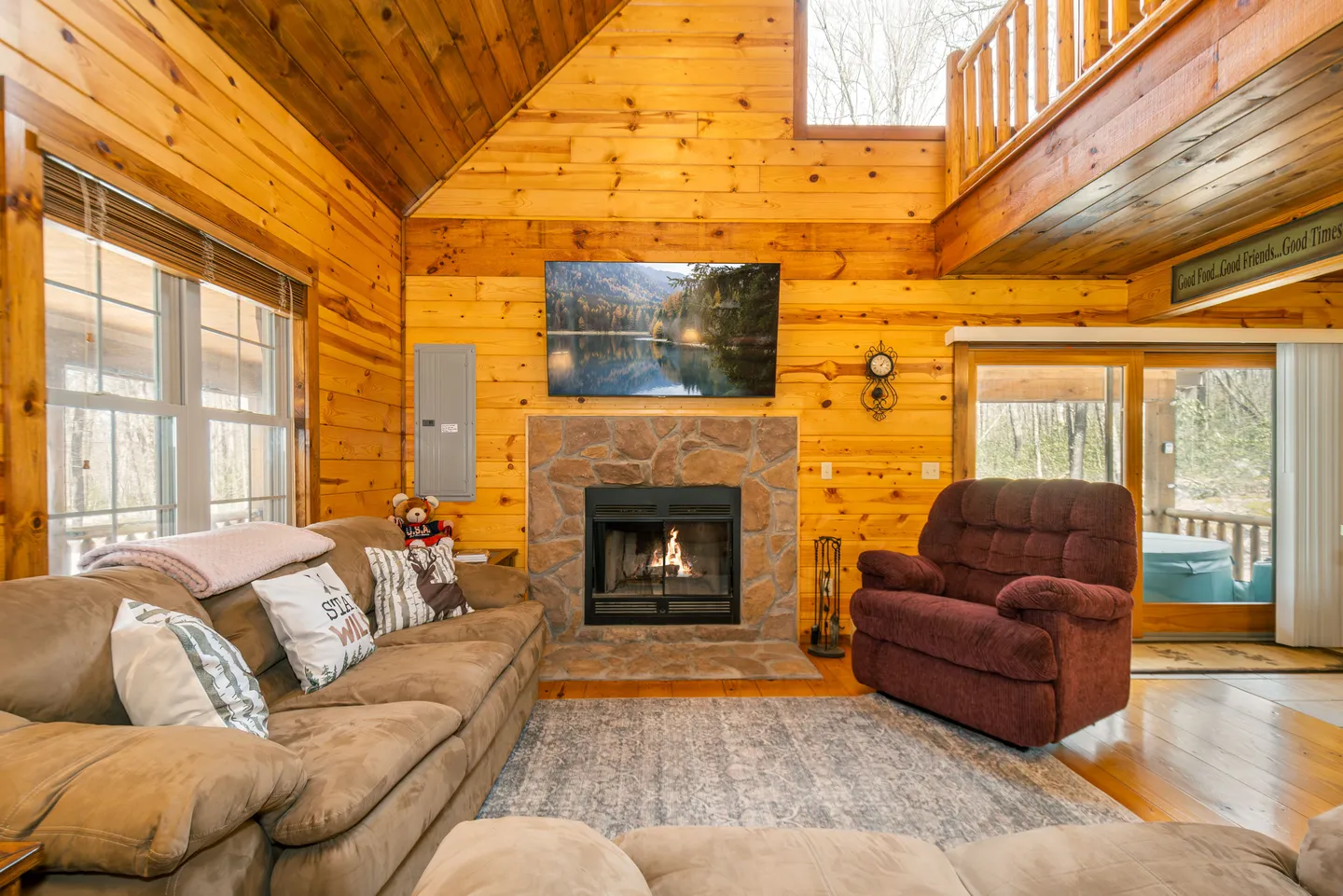 Living room with wood-paneled walls, stone fireplace with burning fire, wall-mounted television, and seating area.
