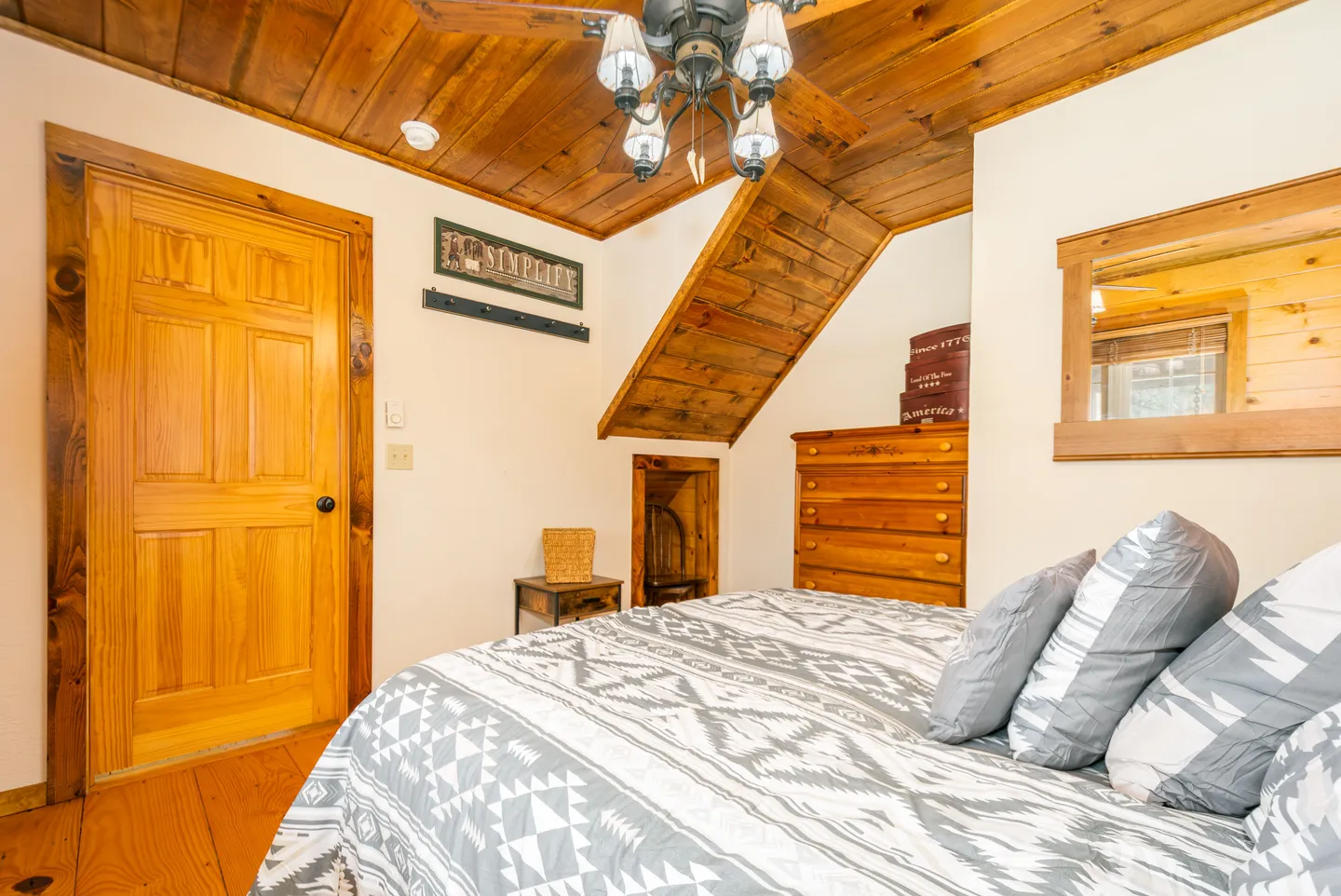 Bedroom featuring a bed with patterned bedding, wood-plank ceiling, ceiling fan with light, and wooden furniture.