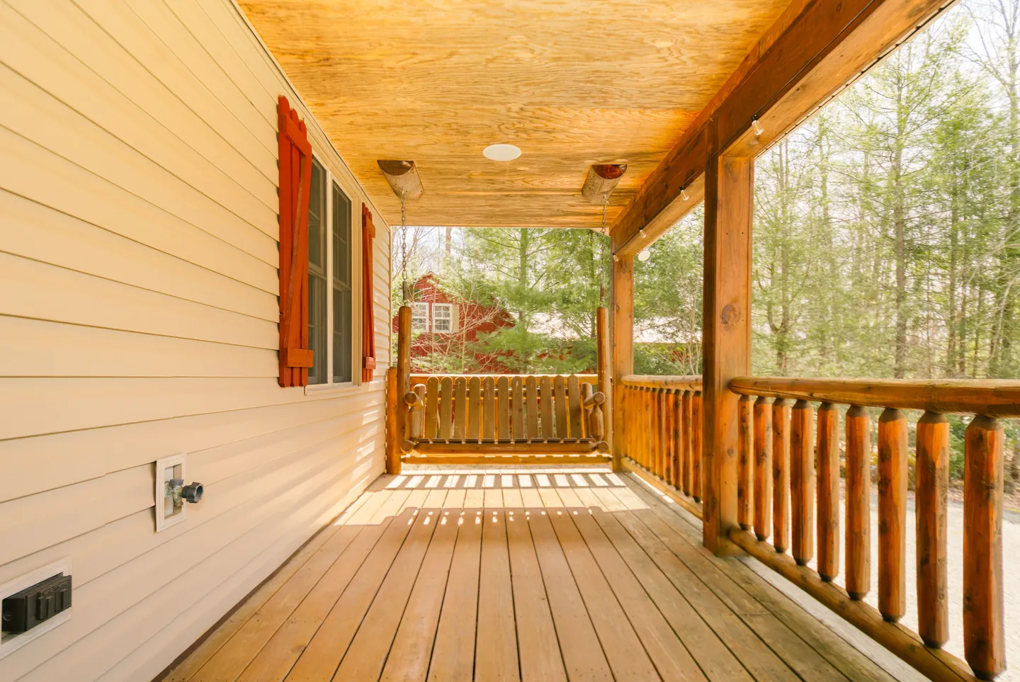 A covered wooden porch featuring a log-style porch swing, wooden railings, and view of surrounding trees.