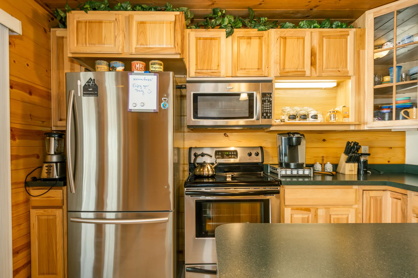 Kitchen with light wood cabinetry, stainless steel appliances, and dark green countertops.