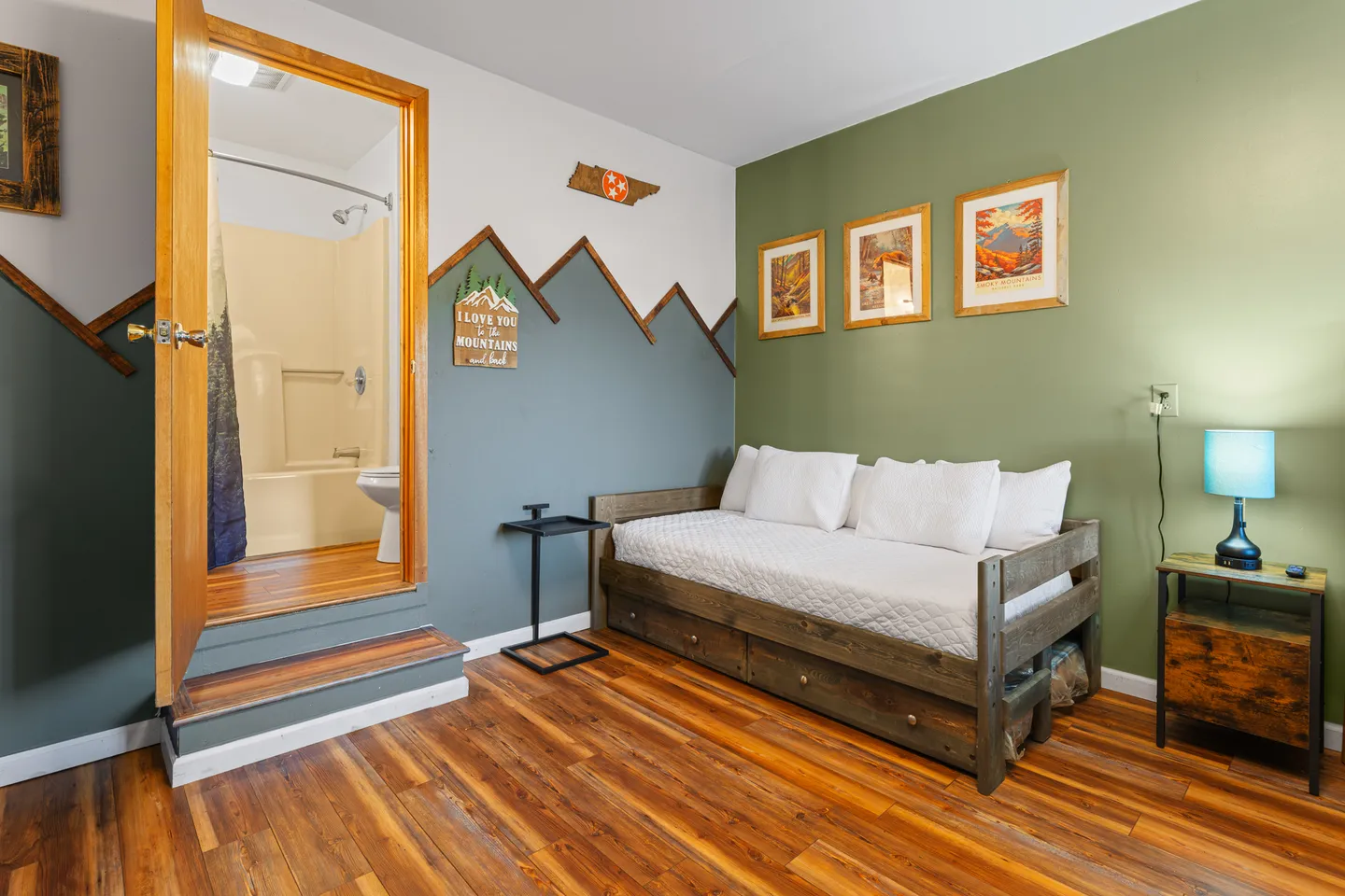 Bedroom featuring a wooden daybed with drawers, mountain-themed wall art, and steps leading to an en-suite bathroom.