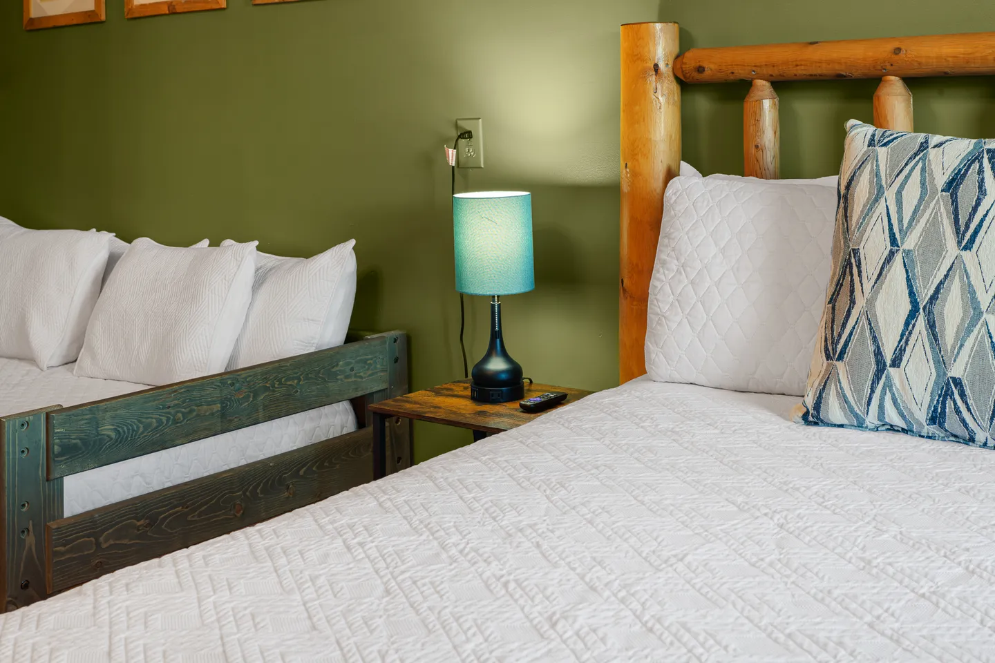 Bedroom with olive green walls, a rustic log bed, and an adjacent daybed separated by a small nightstand with a lamp.