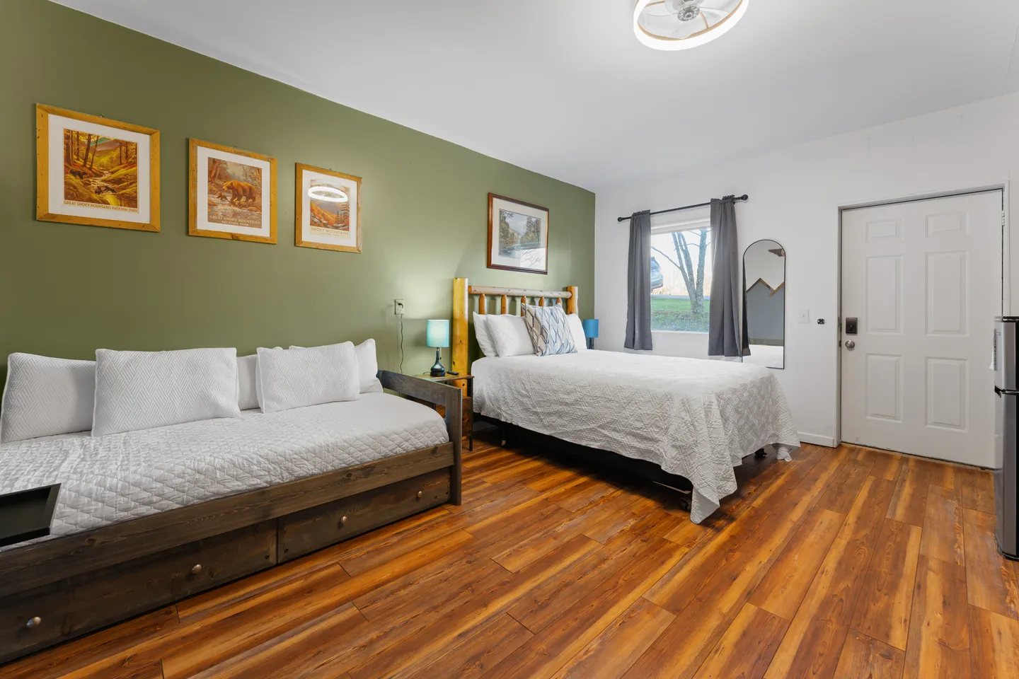 Bedroom featuring wood-look flooring, an olive green accent wall, a daybed, and a bed with a rustic wooden headboard.