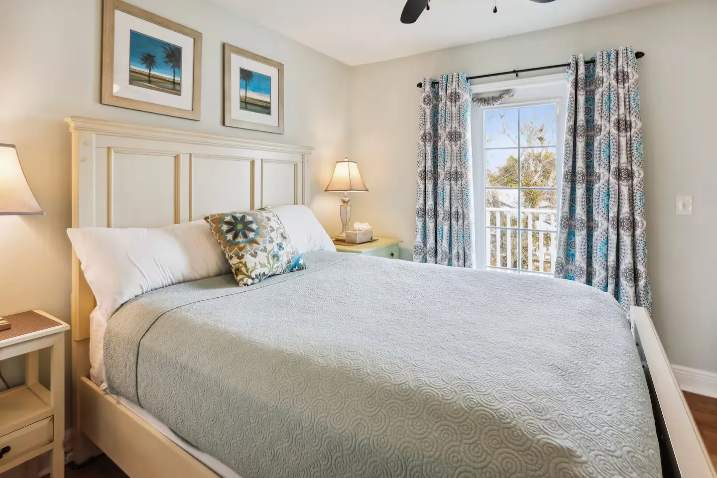Bedroom featuring a light-colored wooden bed, bedside tables with lamps, and a glass door leading to a balcony.