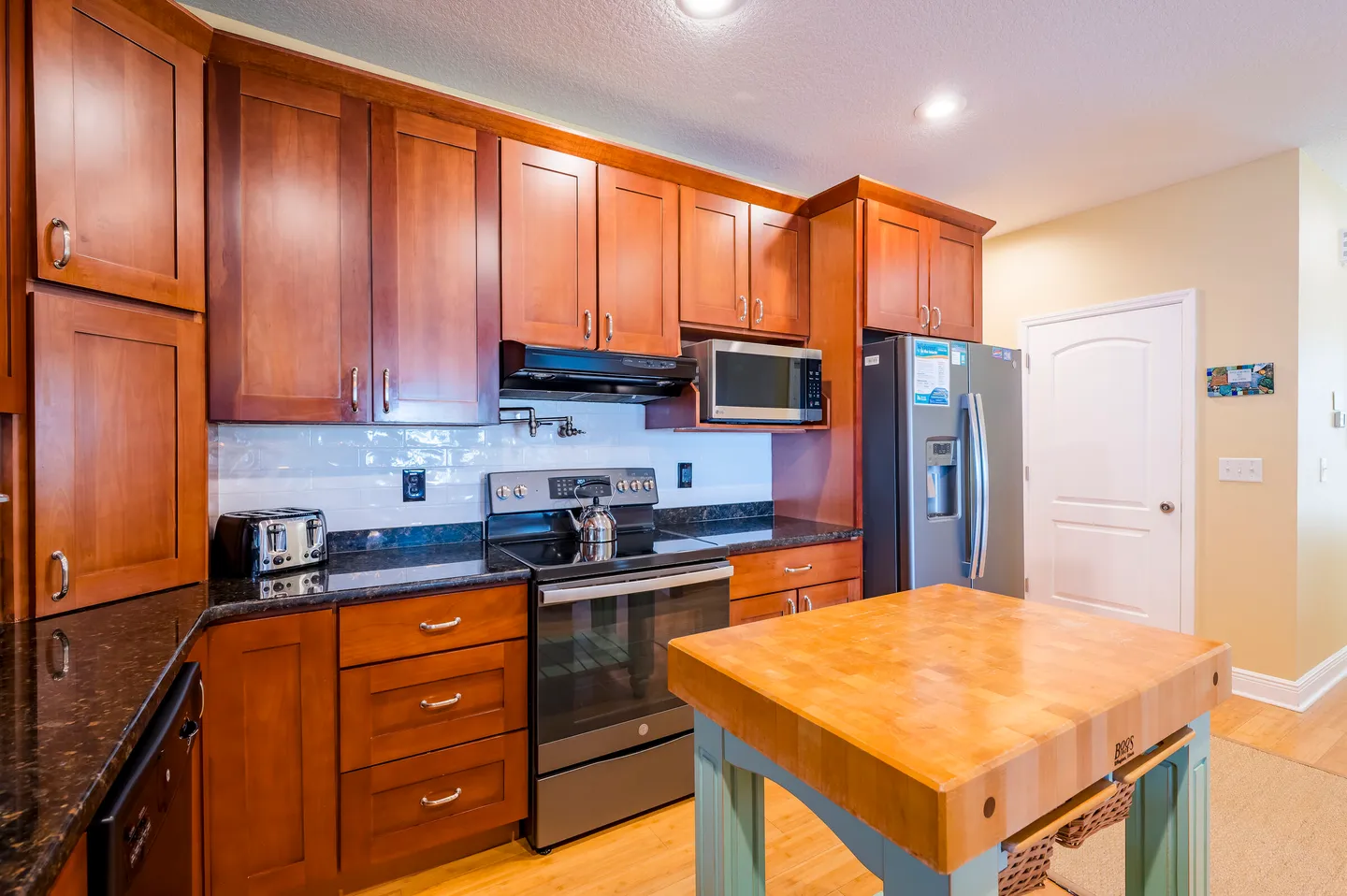 Kitchen with wooden cabinetry, dark countertops, stainless steel appliances, and a butcher block island.