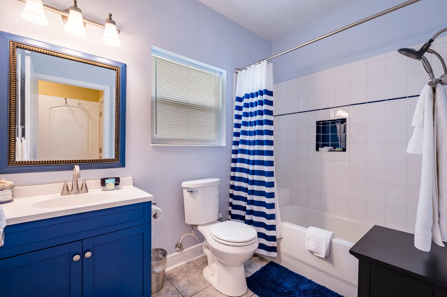 Bathroom with a blue vanity, mirror, toilet, and combination bathtub and shower with blue and white striped curtain.