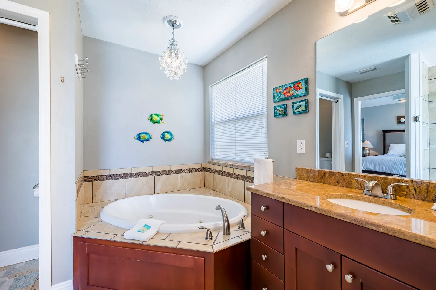 Bathroom featuring a corner soaking tub beneath a crystal chandelier, with a vanity counter and mirror reflecting an adjacent bedroom.