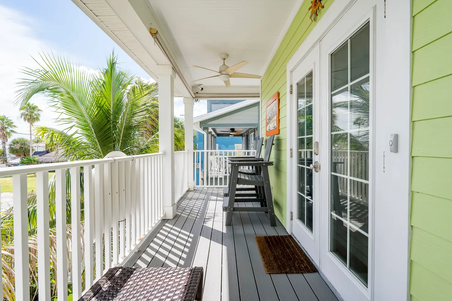 A covered balcony with white railings, a ceiling fan, outdoor seating, and green exterior siding.