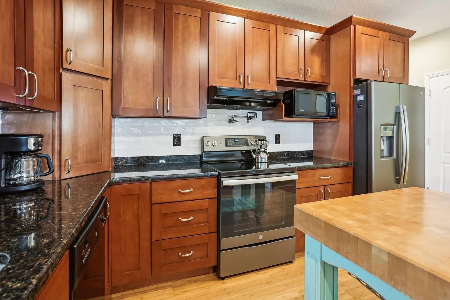 Kitchen with warm wood cabinetry, dark speckled granite countertops, a stainless steel range, and a butcher block island.