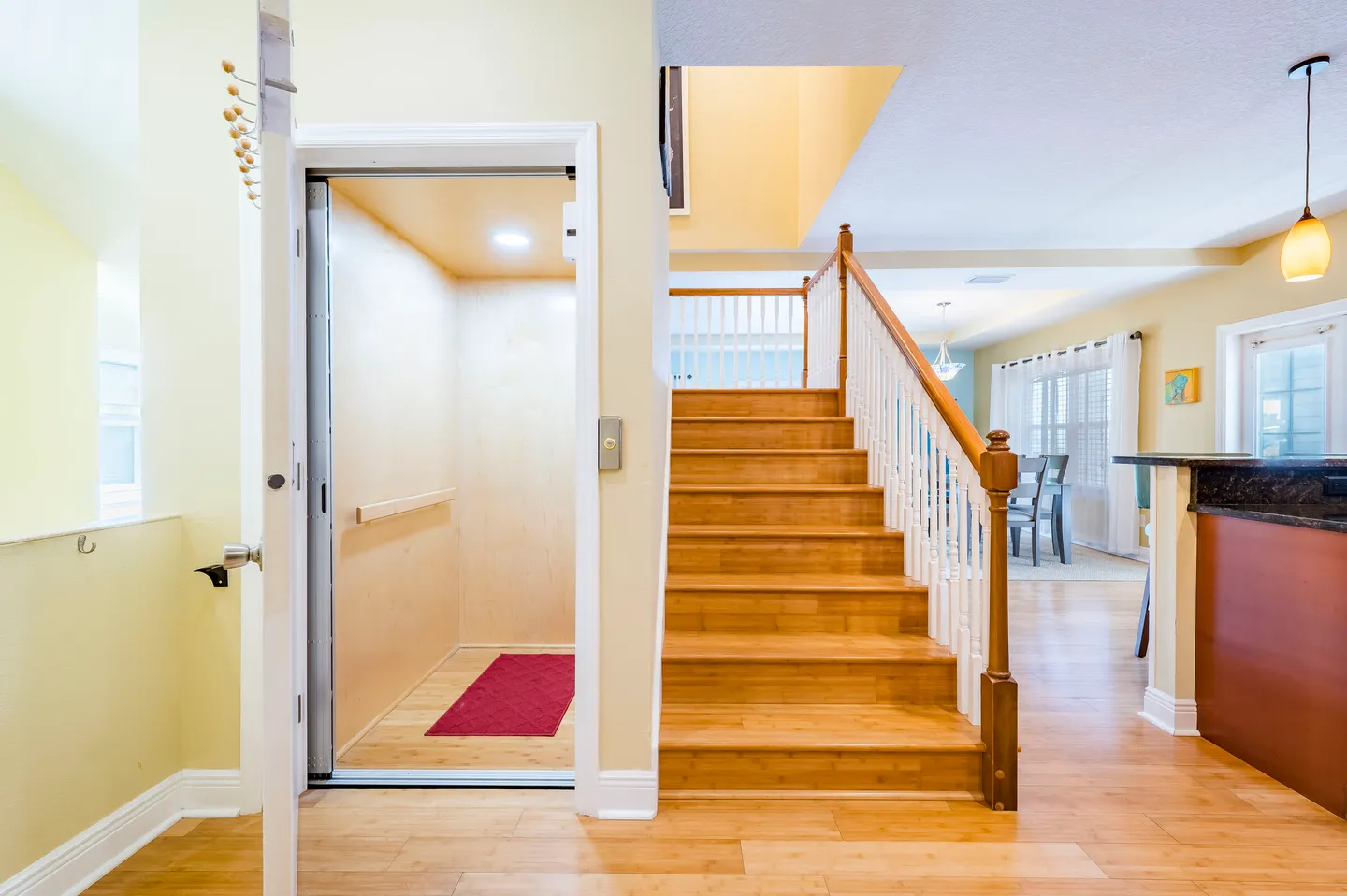 Open residential elevator next to a wooden staircase with white spindles leading up to the second floor.