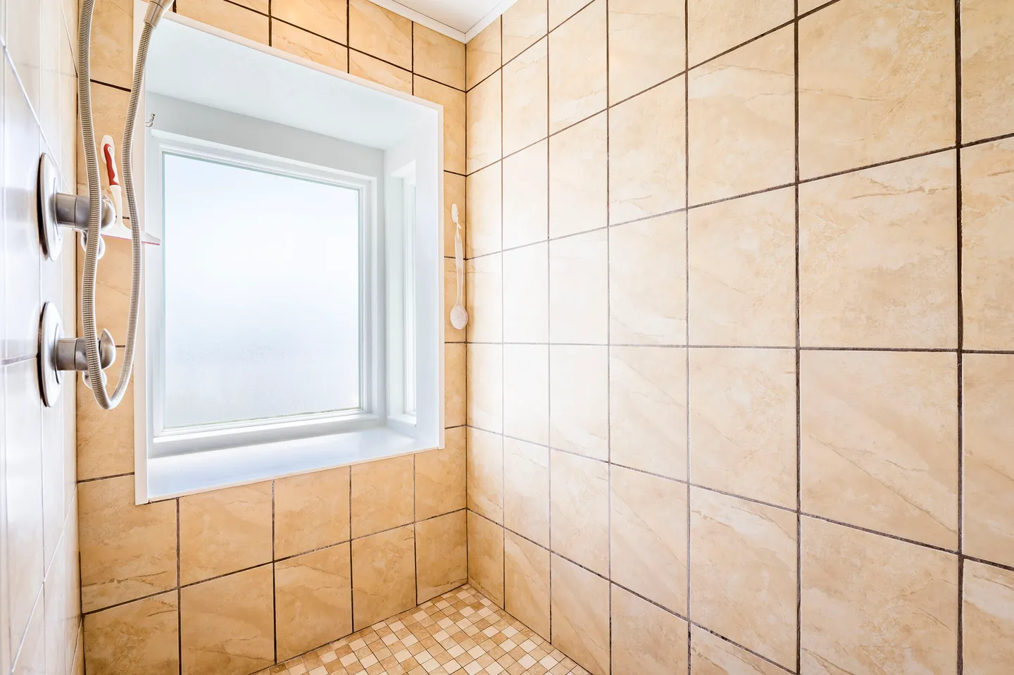 Tiled walk-in shower stall with a frosted glass window and handheld showerhead.
