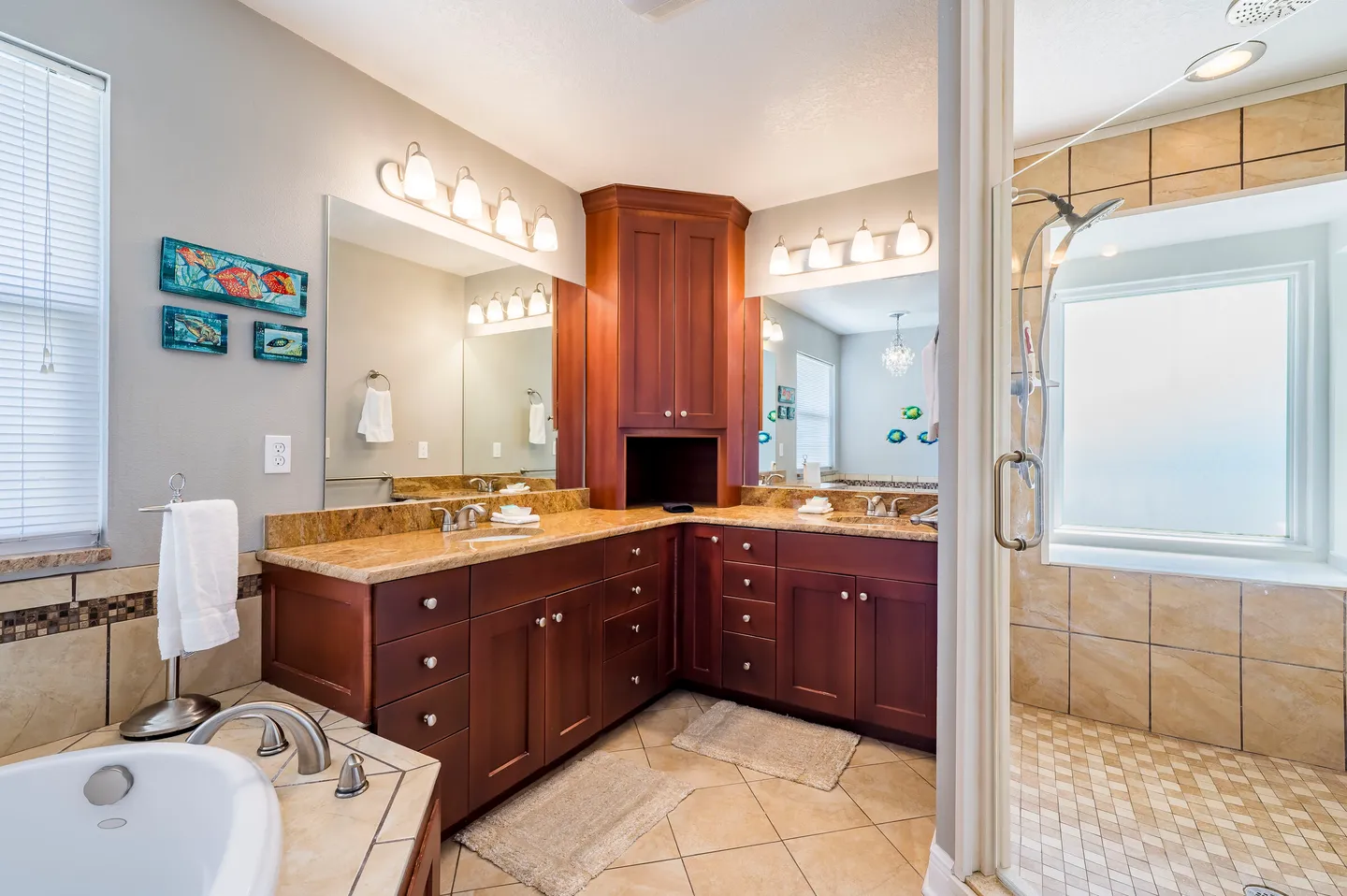 Bathroom with double vanity, corner tower cabinet, tiled walk-in shower, and bathtub edge.