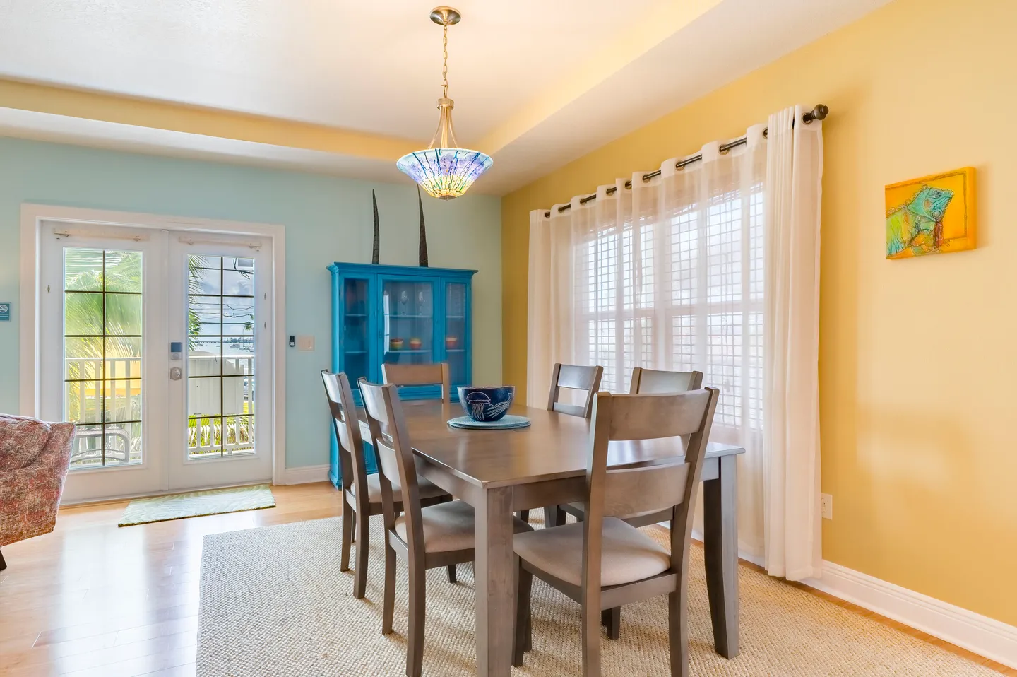 Dining room featuring a wooden table with chairs over an area rug, beneath a stained-glass chandelier and next to glass French doors.