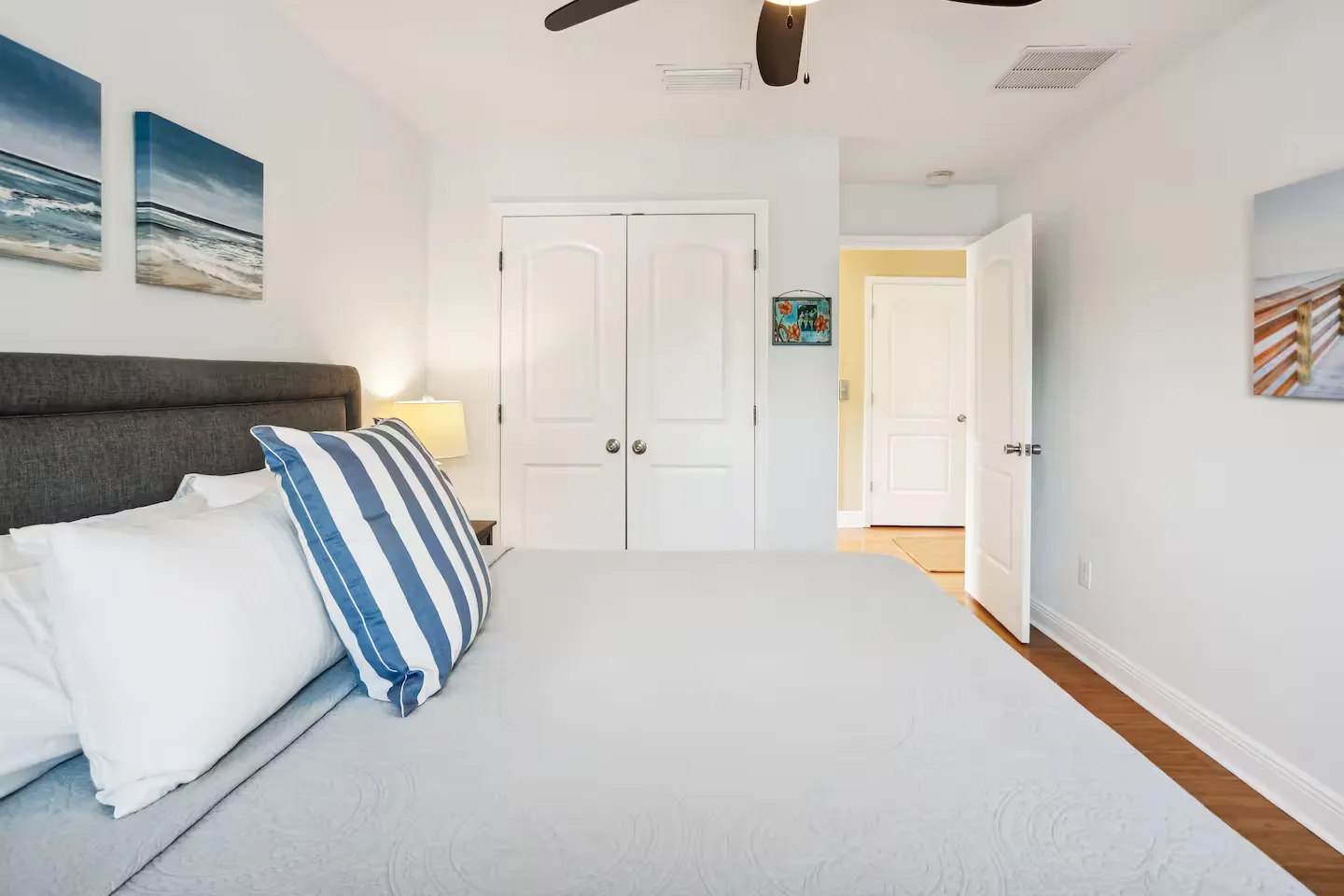 Bedroom with a bed, dark gray upholstered headboard, white closet doors, and open doorway showing a hallway.