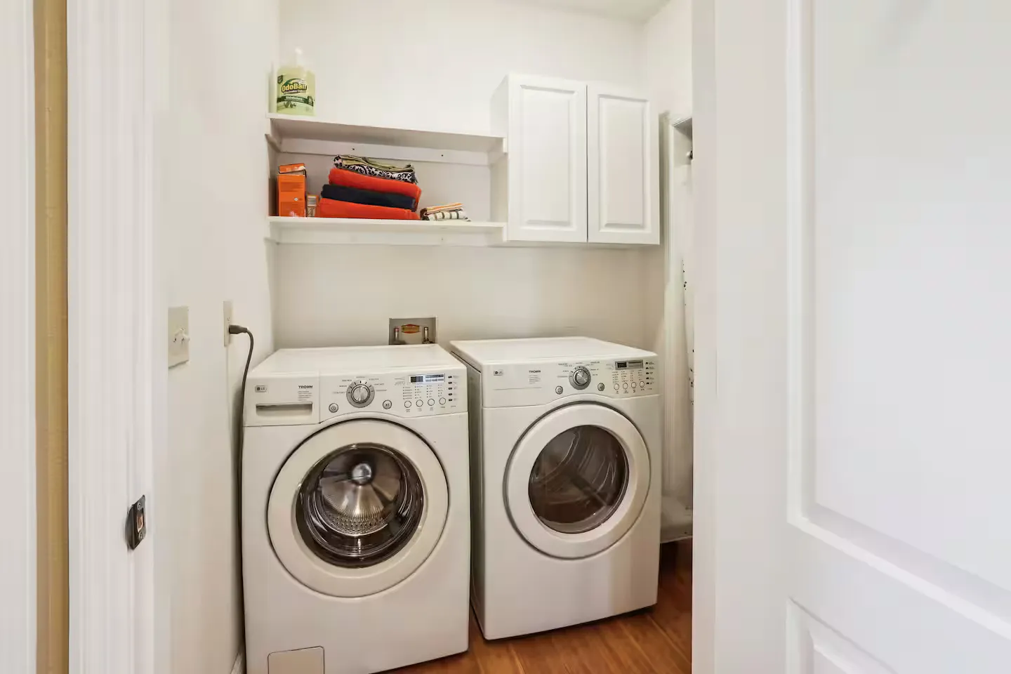 Front-loading white washer and dryer in a laundry closet with shelving and wall cabinets above.