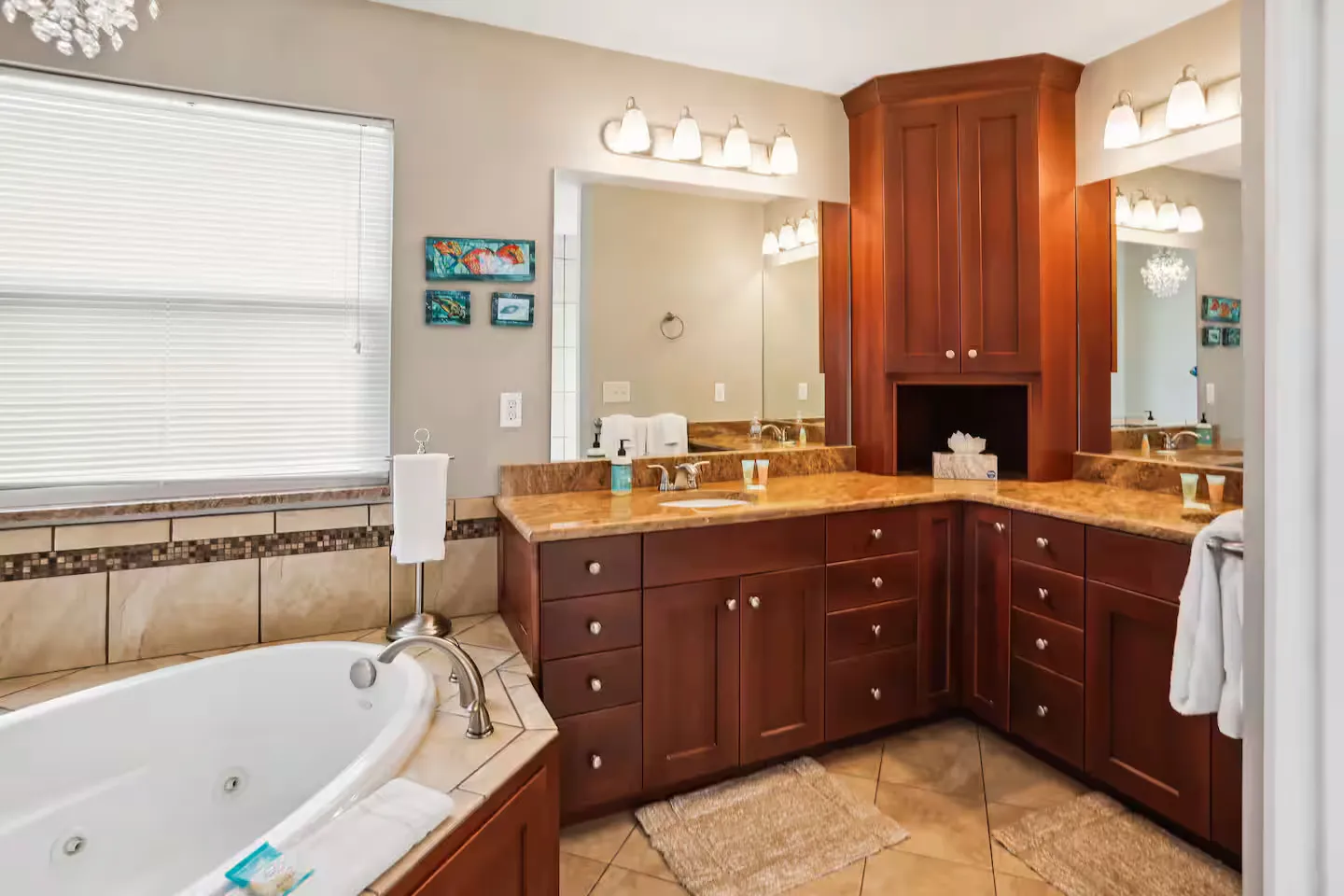 Bathroom with a corner soaking tub next to an L-shaped wooden vanity with granite countertops and overhead vanity lights.