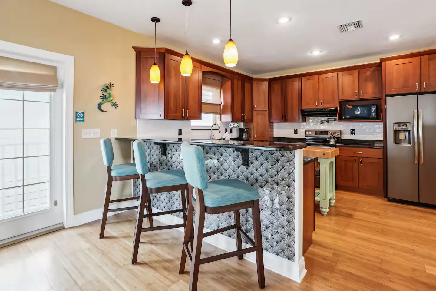 Kitchen counter breakfast bar with three blue upholstered stools, pendant lights, and dark wood cabinets in the background.
