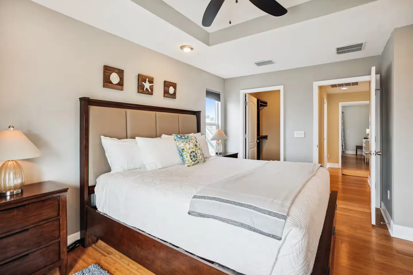 Bedroom featuring a dark wood bed with an upholstered headboard, recessed tray ceiling, and hardwood floors leading to a closet and hallway.