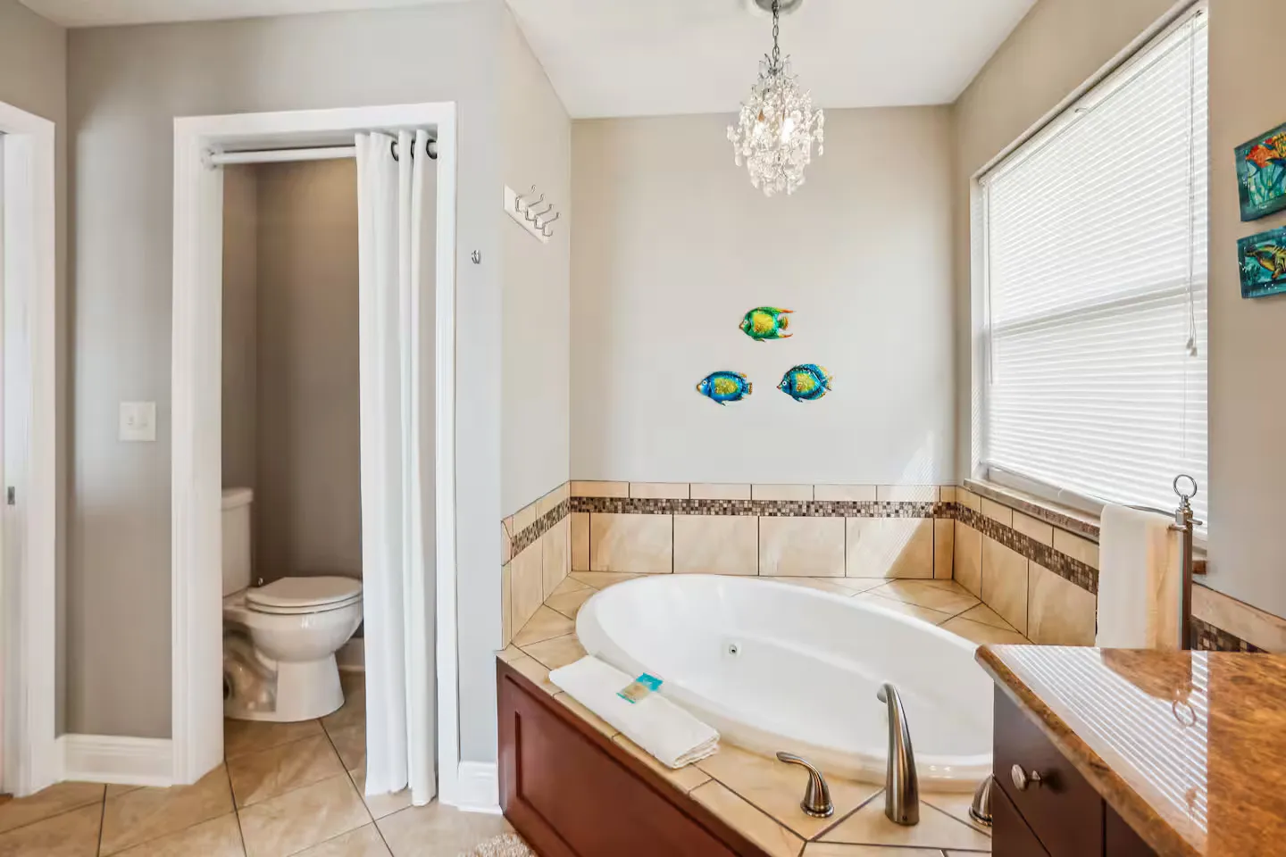 Bathroom featuring a corner soaking tub with tile surround, a small chandelier, and a toilet alcove with a curtain.