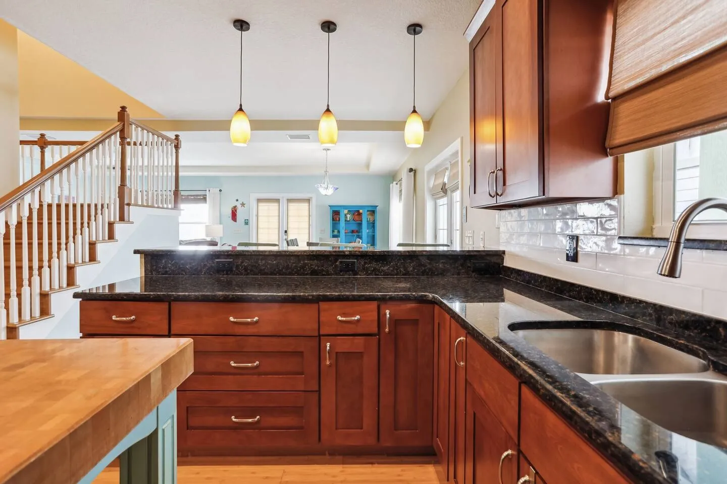 Kitchen counter with dark speckled countertops and wood cabinetry overlooking an open living area and staircase.