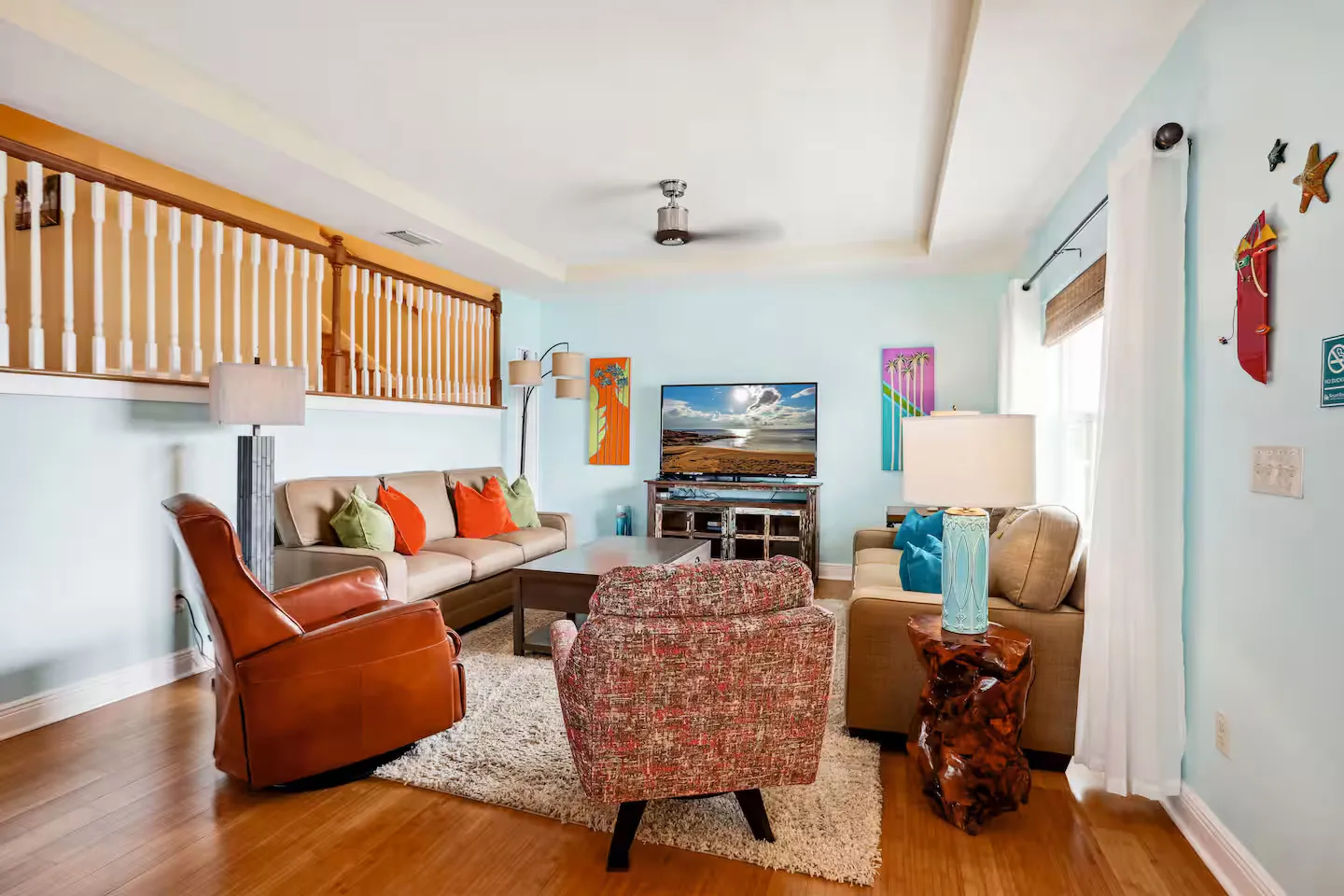 Living room with light blue walls, two sofas, armchairs, a coffee table, a flat-screen TV, and tray ceiling with a ceiling fan.