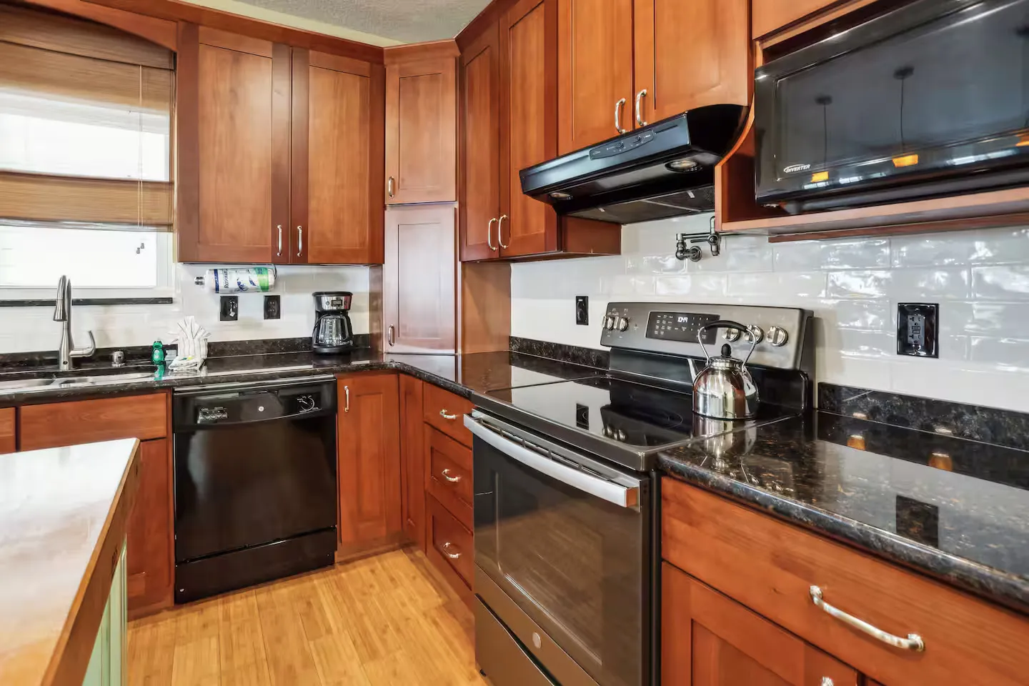 Kitchen with warm wood cabinetry, dark countertops, a black dishwasher, and a freestanding electric range.
