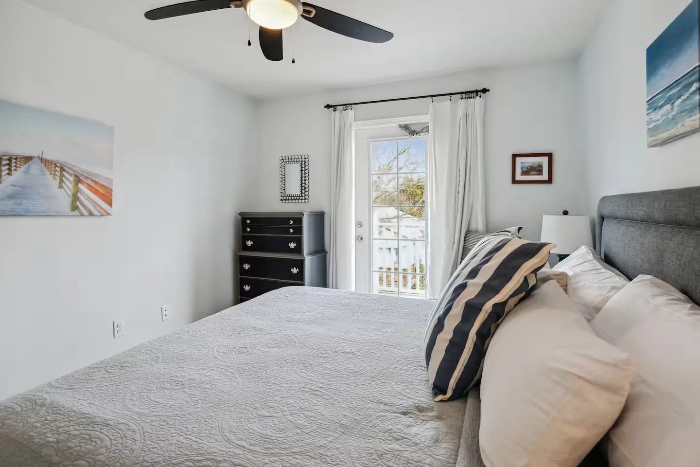 Bedroom with a made bed, dark dresser, ceiling fan, and glass door leading to an outdoor deck or balcony.