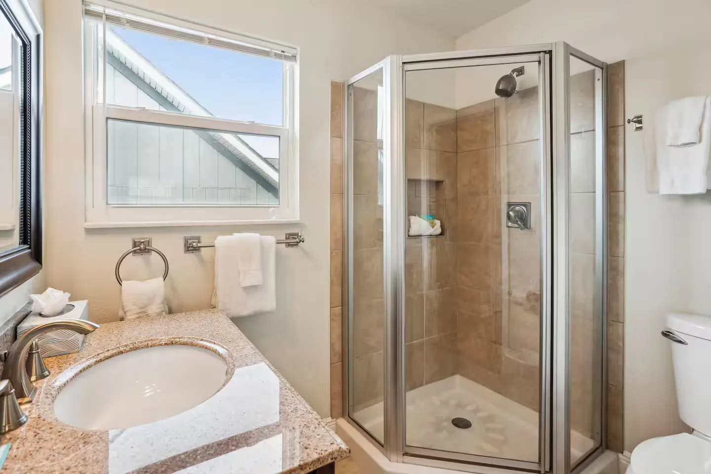 Bathroom featuring a vanity with speckled countertop and an angled glass-enclosed shower stall with tan wall tiles.