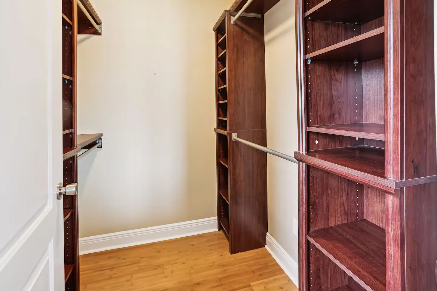 Walk-in closet with dark wood shelving units, hanging rods, and light-toned flooring.