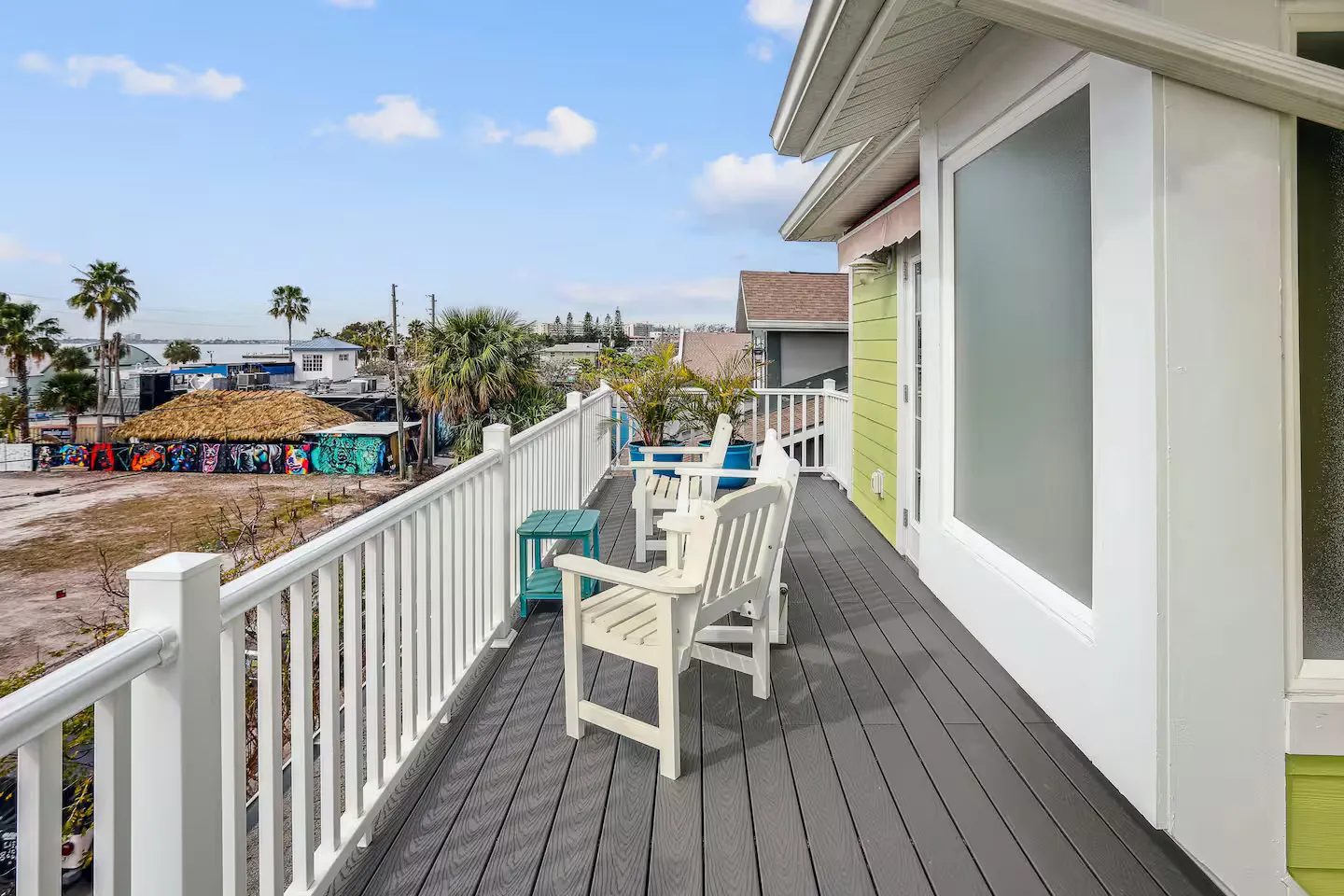 Elevated outdoor balcony with white railing, grey composite decking, and white armchairs overlooking the surrounding neighborhood.