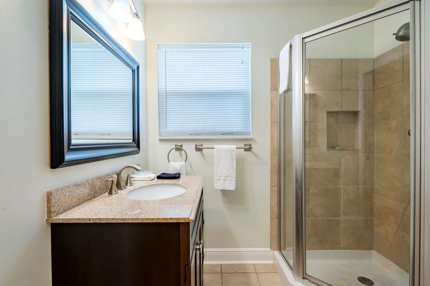 Bathroom featuring a dark wood vanity with a stone countertop, a framed mirror, and a glass-enclosed walk-in shower with beige tile.