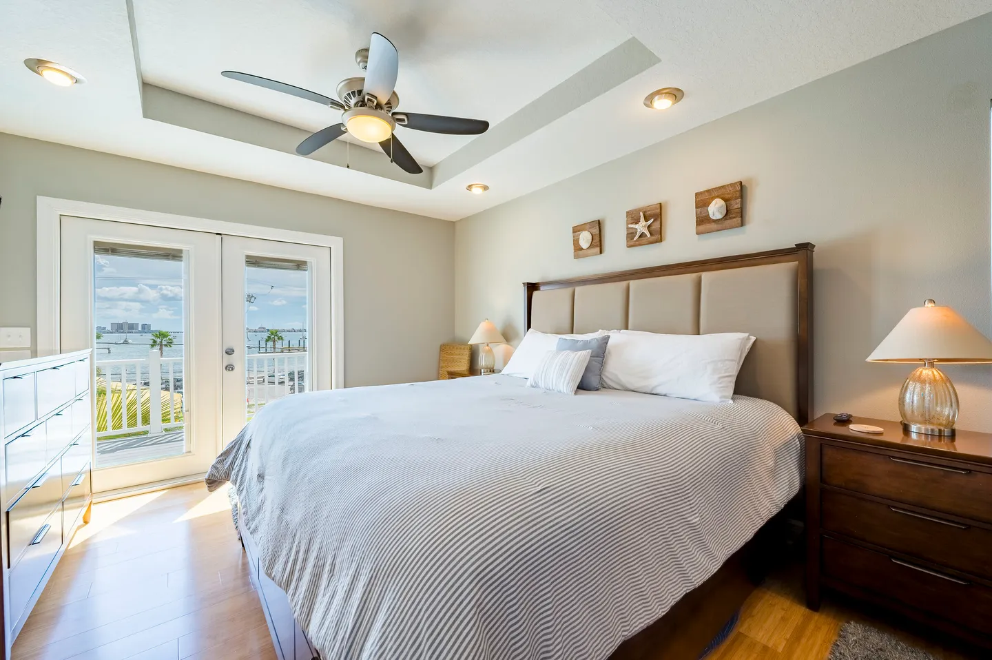 Bedroom with a large bed, ceiling fan, and glass doors opening to a balcony with water views.
