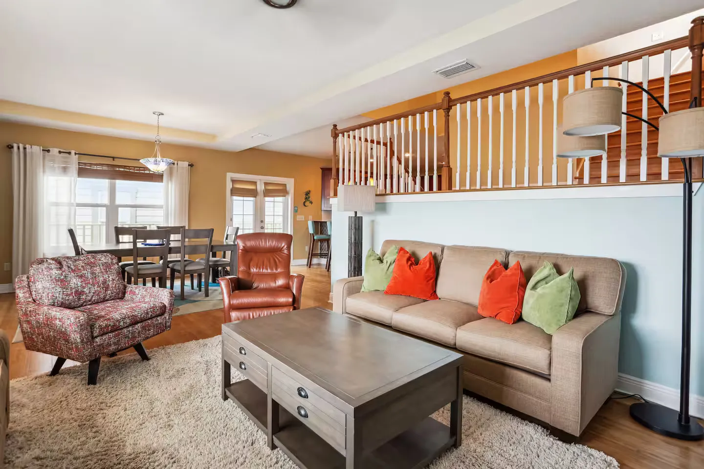 Open living area with a sofa, wooden coffee table, armchair, and an adjacent dining area beside a staircase with white spindles.