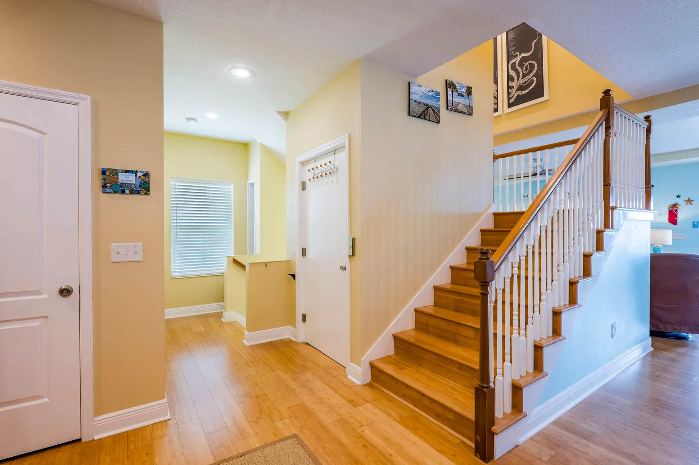 Entryway and hallway featuring light wood flooring, light yellow walls, and a wooden staircase leading up with white spindles.