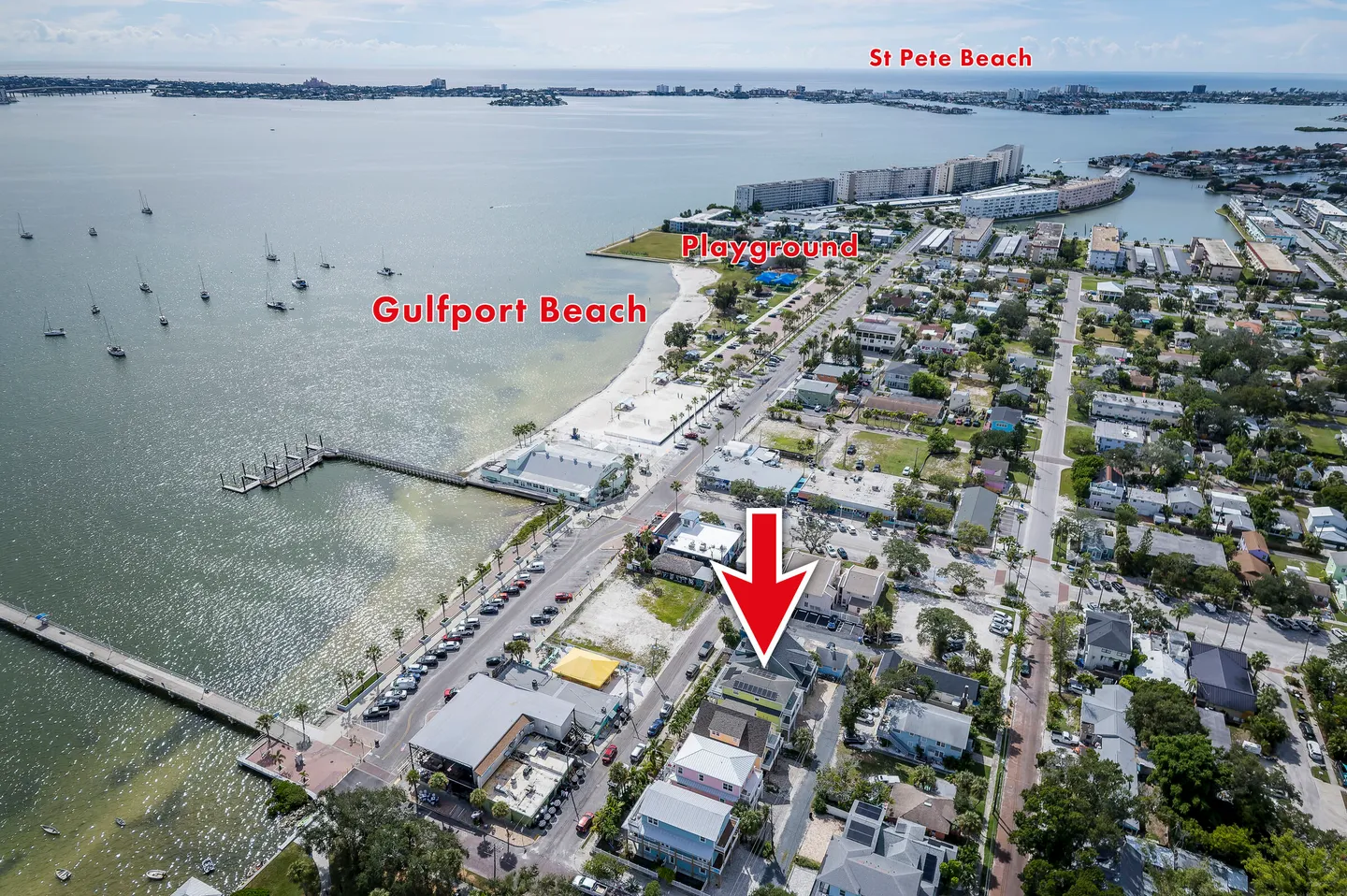 Aerial view showing coastal neighborhood with a red arrow pointing to a residential building near the shoreline, beach, and piers.