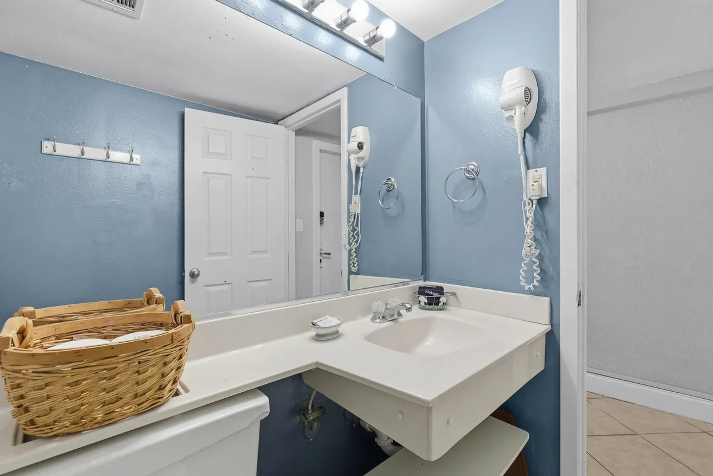 Bathroom vanity with a white sink, large mirror, wall-mounted hair dryer, and light blue walls.
