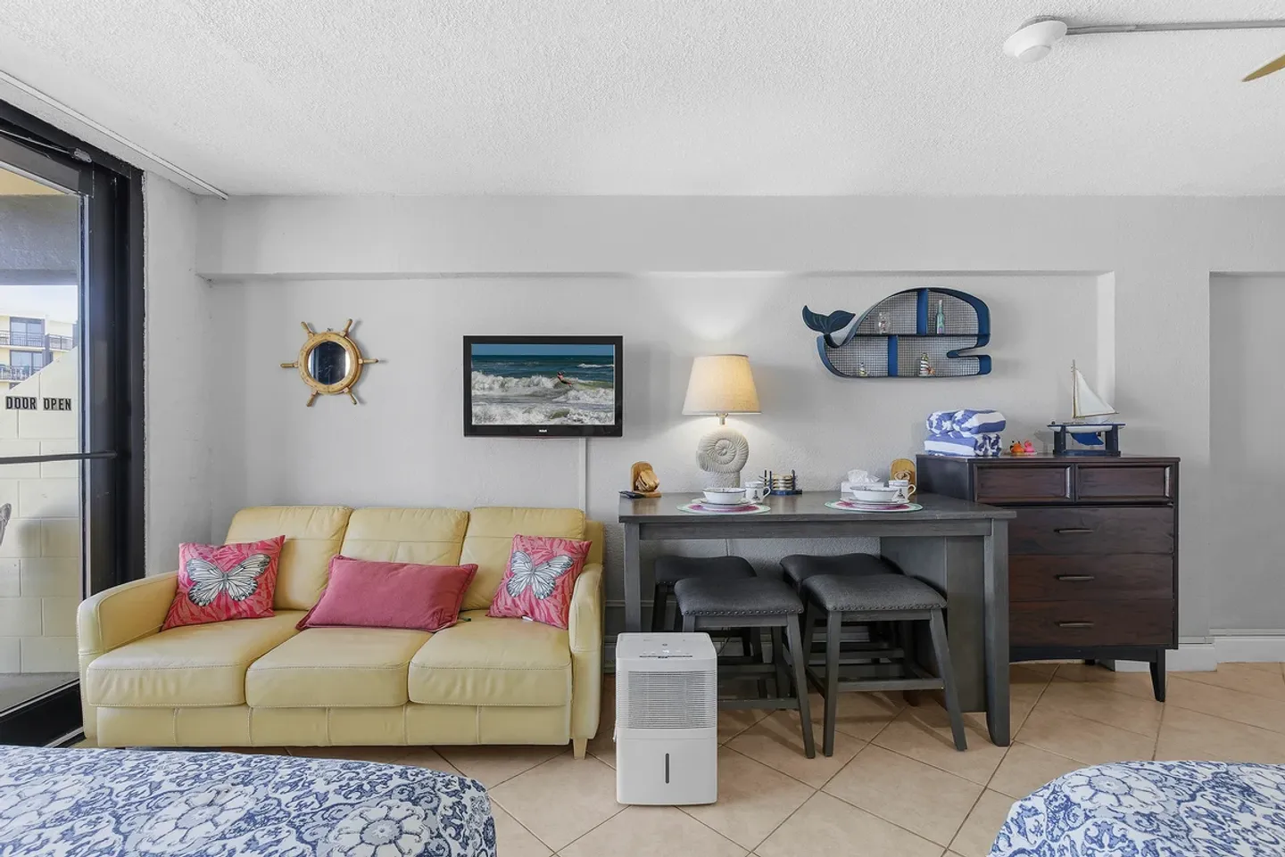 Living and dining space featuring a yellow sofa, a table with backless stools, and tiled flooring.