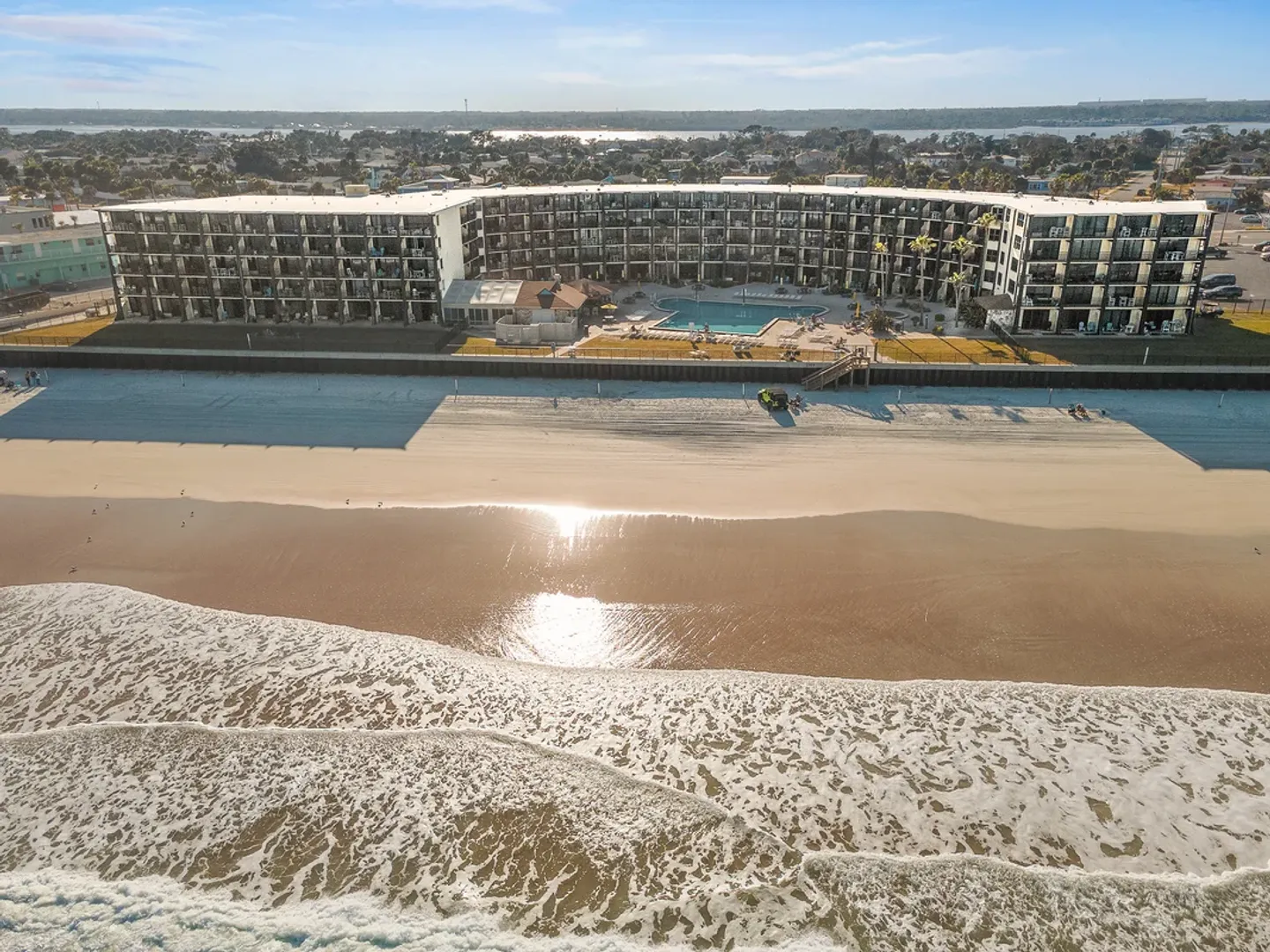 Aerial view of a beachfront condominium complex with a swimming pool facing the ocean and sandy beach.