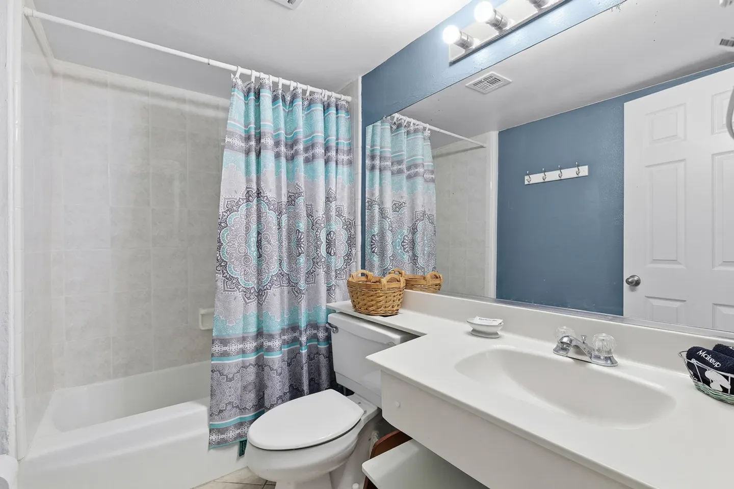 Bathroom with a bathtub shower combination, patterned shower curtain, toilet, and vanity with large mirror.