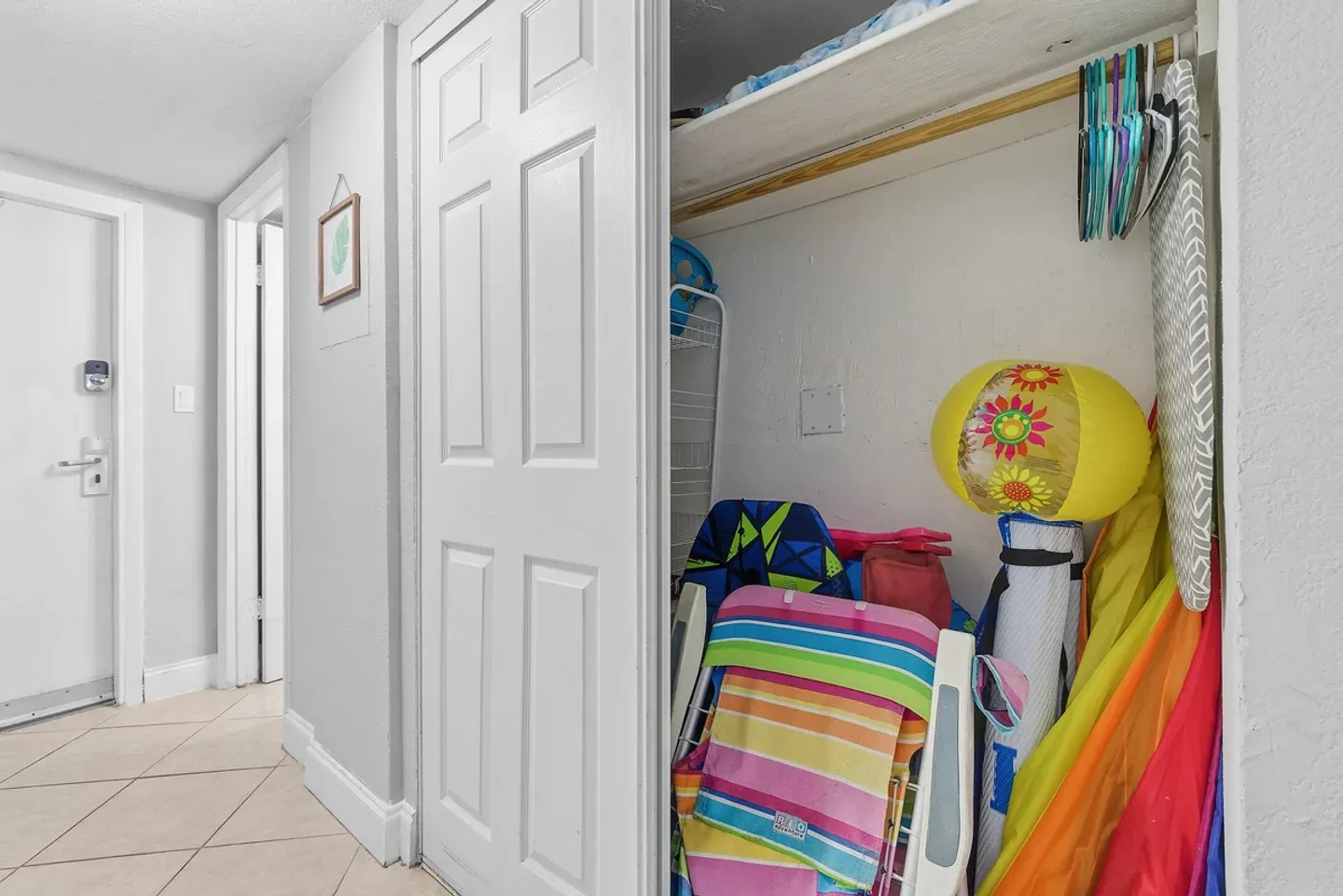 Open hallway closet stocked with colorful beach chairs, an umbrella, an ironing board, and beach gear.