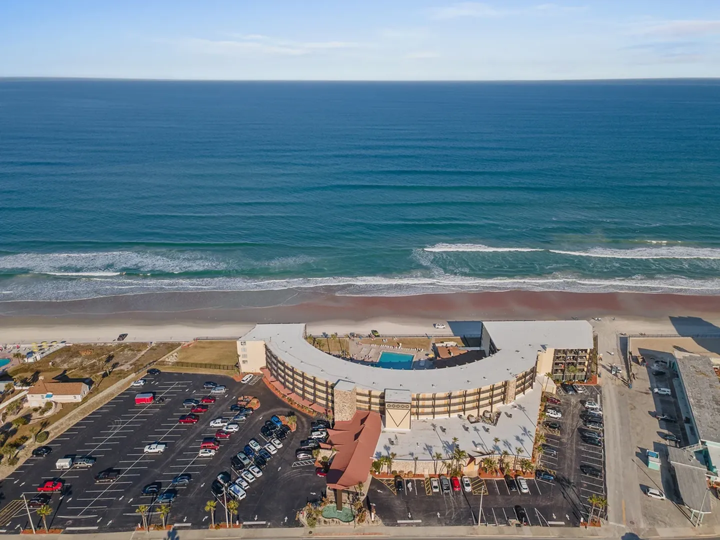 Aerial view of a curved oceanfront resort building overlooking the beach and ocean.