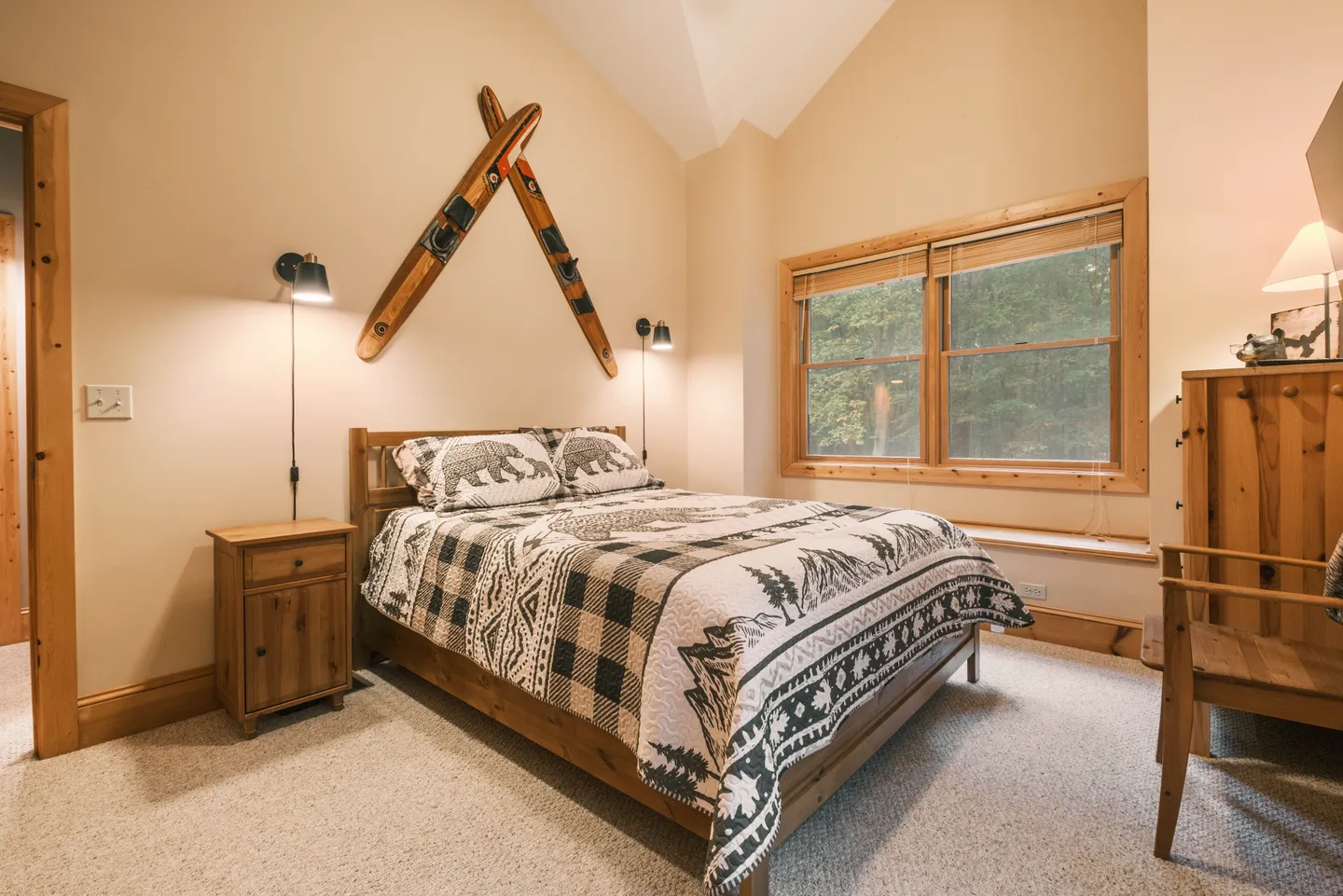 Bedroom with a wooden bed, patterned quilt, wall-mounted skis, and a window framed in wood.