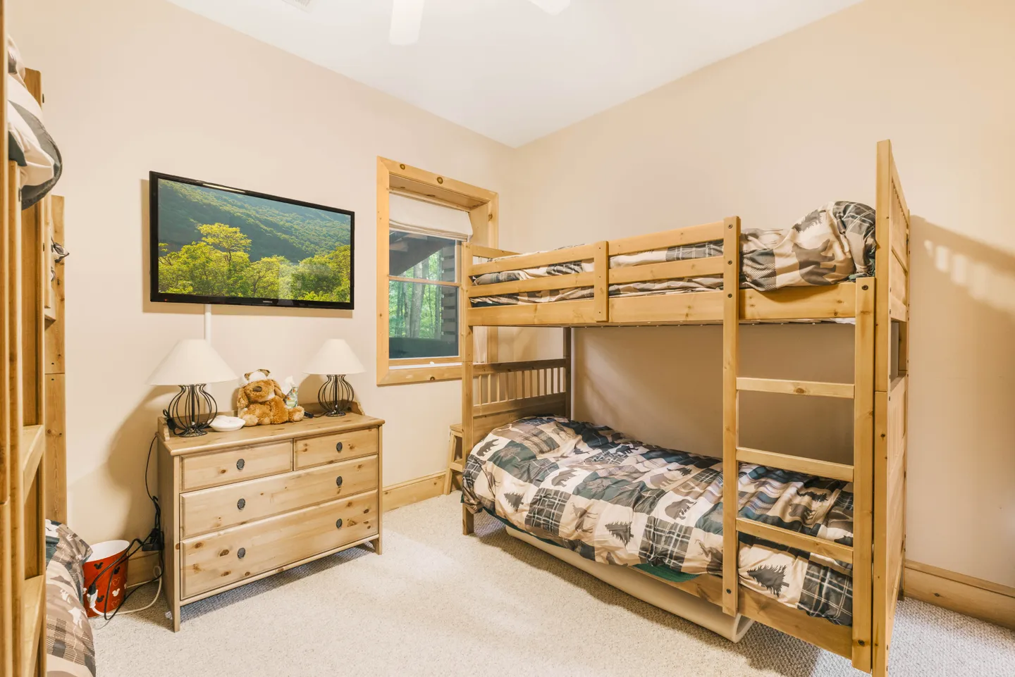Bedroom with carpeted floor, wooden bunk beds, a wooden dresser with lamps, and a wall-mounted TV.