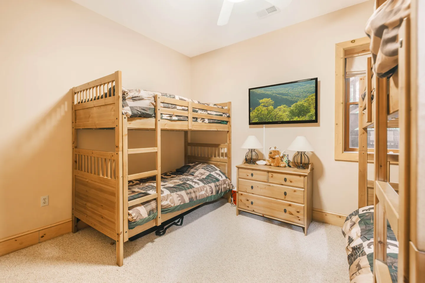 Bedroom featuring wooden bunk beds, a wooden dresser with lamps, a wall-mounted TV, and light carpeting.