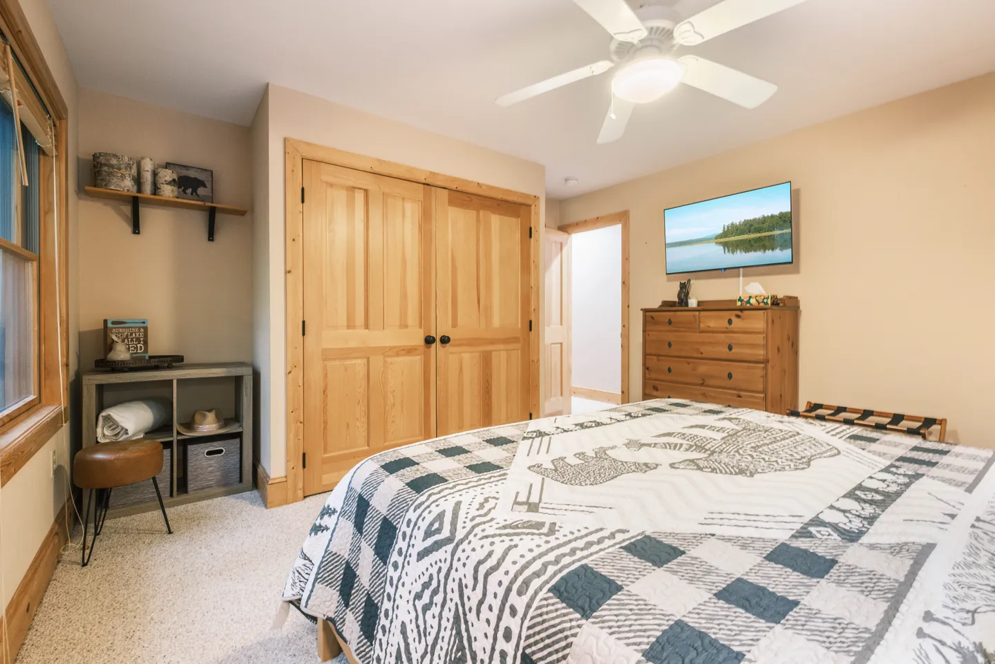 Bedroom with a patterned quilt on the bed, wooden closet doors, a dresser, and a wall-mounted TV.