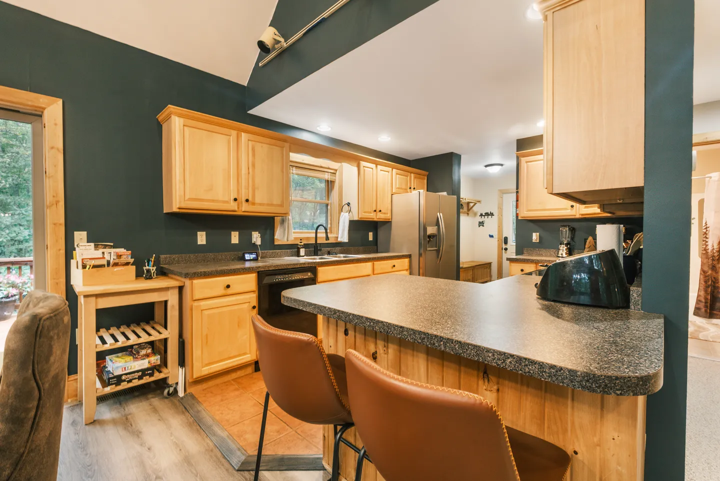 Kitchen with dark green walls, light wood cabinets, dark speckled countertops, and an island with brown barstools.