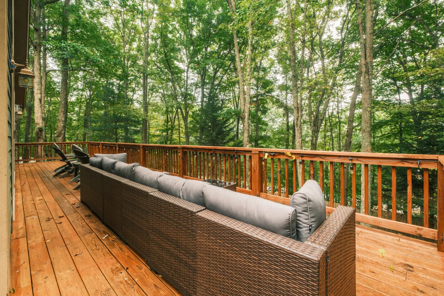 Outdoor wooden deck with a large wicker sofa looking out toward dense green woods.