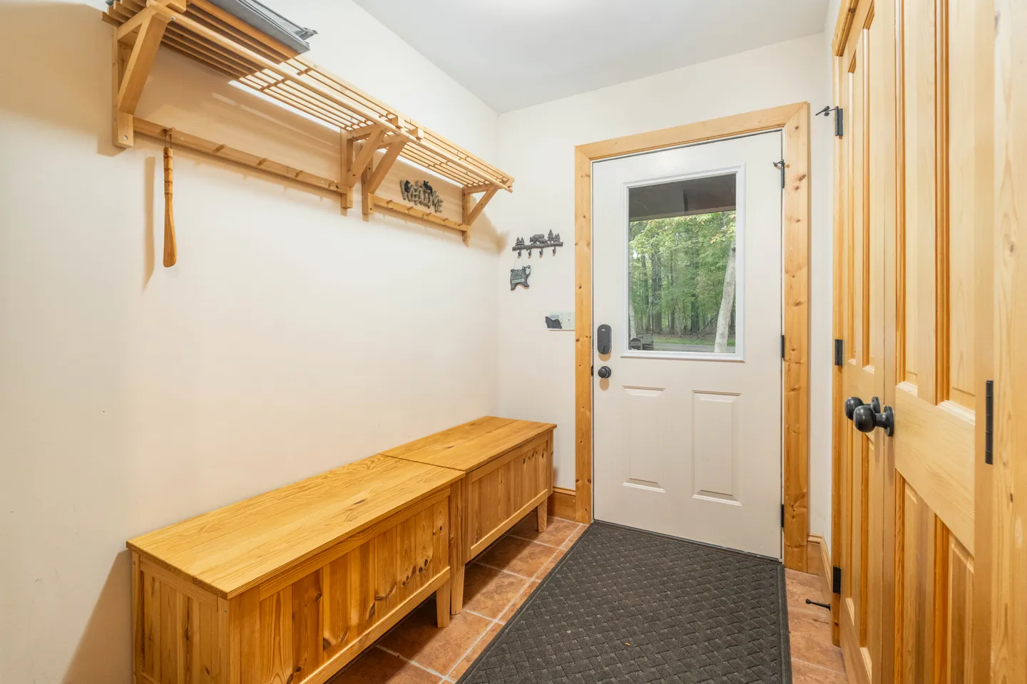 Entryway with an exterior door featuring a glass window, wooden storage benches, and an overhead wooden shelf.